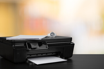 Compact laser printer on black desk against blurred background
