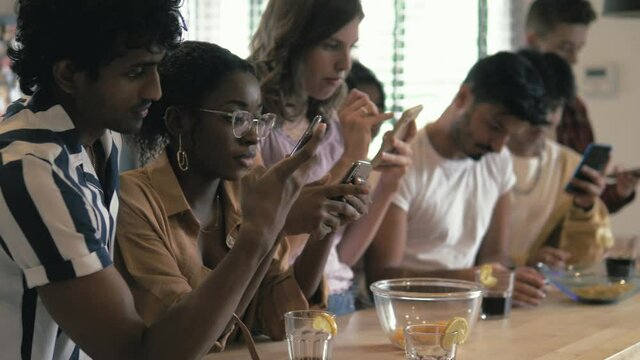 Big group of Young diverse multiracial people sitting together and looking at their phones - Social media concept and addiction, millennials lifestyle