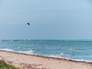 The athlete practices kite board surfing on blue sea waves. Autumn kiteboarding. Fall ocean fun. Extreme sport kitesurfing. Windy weather on the beach.