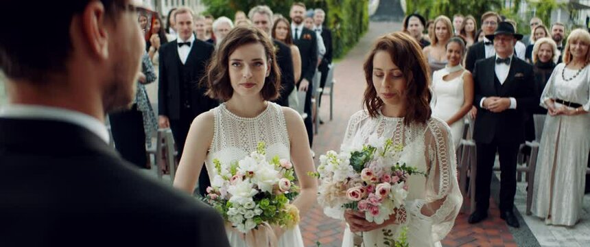 Portrait of two LGBT females lesbians brides kissing during wedding ceremony, guests clapping and cheering. Shot with 2x anamorphic lens