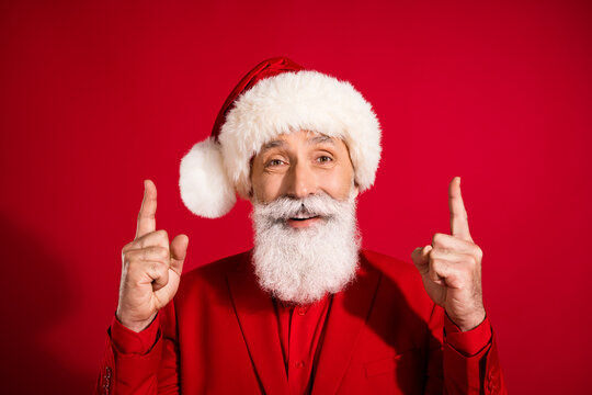 Photo of reliable santa claus indicate forefingers up empty space wear x-mas hat suit on red color background