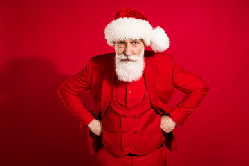 Portrait of attractive strict moody suspicious bearded grey-haired man hands on hips isolated over bright red color background