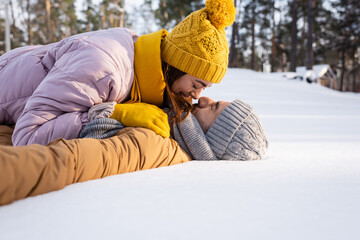 Fototapeta na wymiar Side view of young couple in hats kissing while lying on snow