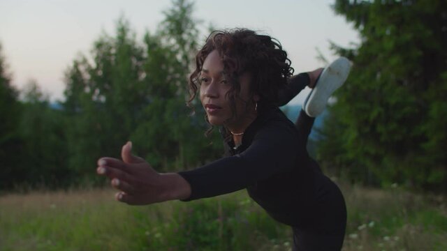Portrait of focused active pretty sporty fit black female practicing yoga dancer pose stretch exercise, developing flexibility in spine shoulders and hamstrings while working out outdoors at sunrise.