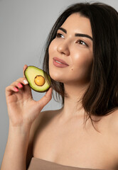 Portrait of female model with clean pure skin smiling, holding a avocado near face. Skin beauty health care concept.