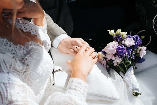 Wedding, marriage concept. Close-up of newlyweds hand with wedding gold rings on top of each other, touching, bridal bouquet of flowers. Cropped image of young married couple