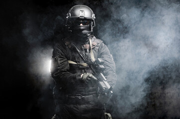 Fototapeta na wymiar Professional special forces fighter in a helmet and with special weapons shrouded in smoke on a black background.