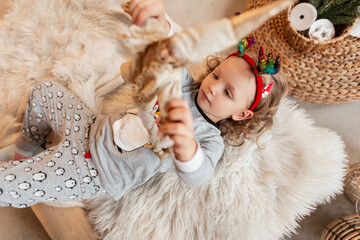 Little beautiful girl child in fashionable pajamas is played with a toy and lies on the bed, top view