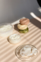 Natural eco handmade facial cream in white jar and soaps, striped shadow background.