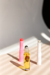 Perfume roller bottle and hygienic lipstick in striped shadow background.