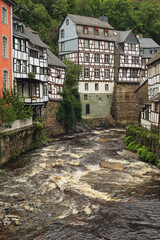 Old half-timbered houses in a village along a river in a valley between the hills.