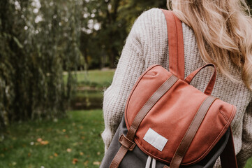 Rear view of a young girl in a knitted jacket. Stylish casual backpack. Autumn fashion. Walking in...