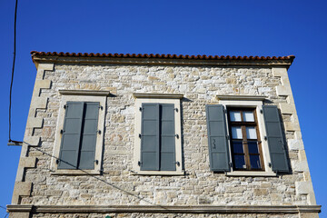 Alte Fassade aus Naturstein mit alten Fensterläden im Sommer bei blauem Himmel und Sonnenschein am...