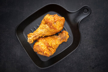 crispy fried chicken drumstick in black skillet pan on dark tone texture background, top view