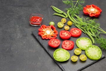 Slices of green and red tomatoes on cutting board. Green beans and dill on table