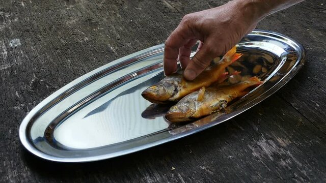 fisherman lays freshly cooked smoked perch on a platter close-up
