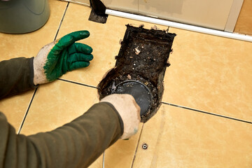 Sewer cleaning. A plumber uses sewer snake to clean blockage clog. Toilet room repair. Canalization pipe. Repairman hands. Bad smell. Dirty water. Metal wire. Yellow color tiles. Plumbing error. DIY - obrazy, fototapety, plakaty