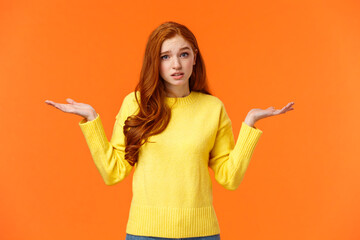 Perplexed cute redhead girl, shrugging with raised arms and looking confused, dont know answer,...