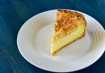 An appetizing piece of sweet cottage cheese pie on a white plate on a blue wooden background