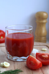 Fresh tomato juice in a glass with tomatoes, salt, garlic and herbs on a wooden board