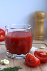 Fototapeta na wymiar Fresh tomato juice in a glass with tomatoes, salt, garlic and herbs on a wooden board