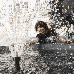 Happy woman by the fountain catches water droplets.Blurred  black white image.