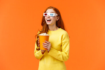Girl eating popcorn, smiling amused as staring at large screen watching movie at cinema, open mouth thrilled, wear 3d glasses on fantasy film theatre, standing orange background
