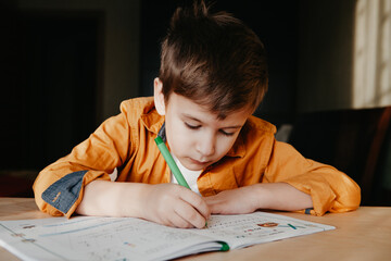 Cute 7 years old child doing his homework sitting by desk