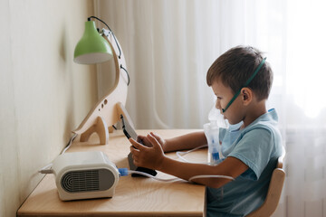 Child siting by table and watching cartoon on tablet during inhalation with nebulizer