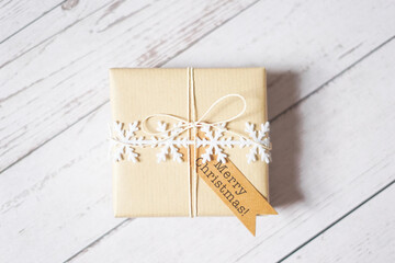 Christmas present on white wooden background. Winter holiday craft, decoration, brown paper, twine, snowflake ribbon, tag. Sustainable gift wrapping. Merry Christmas.