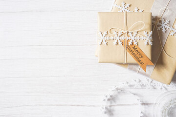 Christmas presents on white wooden background. Winter holiday craft, decoration, brown paper, twine, snowflake ribbon. Sustainable gift wrapping. Merry Christmas. Empty space for text. Copy space.