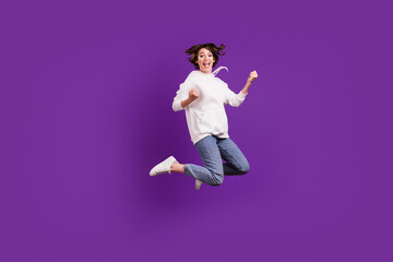 Full size photo of young excited cheerful girl jumping in triumph victory wear hoodie isolated on purple color background