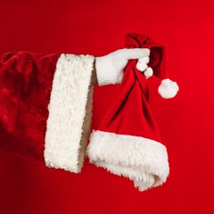 Hand of Santa Claus iholding santa hat on a red background.