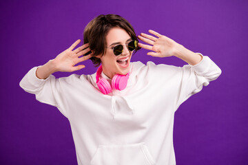 Photo of funky sweet young lady wear white jumper earphones dark glasses dancing isolated purple color background