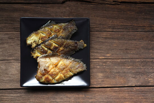 Thai crispy gourami fish , gouramy or Sepat Siam fish or Pla salid in Thai language displayed on the black dish on wooden table in the restaurant for lunch