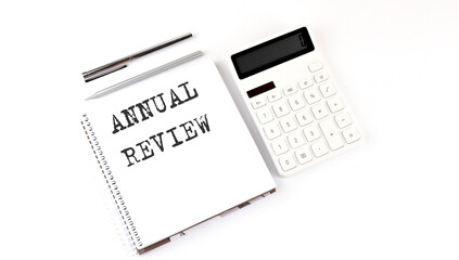 Notepad with text ANNUAL REVIEW with calculator and pen. White background. Business concept