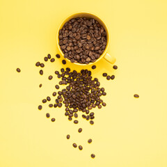 Full cup of coffee beans spread over the yellow surface. Flat lay yellow mug filled with drinking energy for autumn October. Vibrant minimal concept background.