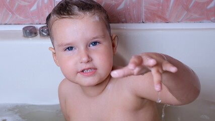 Little playing girl 3 years old bathes and washes with foam on her head in water in the bathroom at home. Baby body care concept, hygiene.