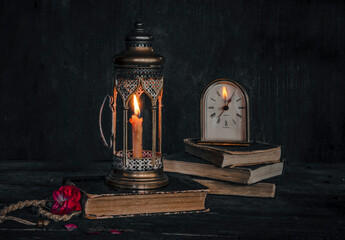 clock on books and a lantern with a candle reflected on the clock face