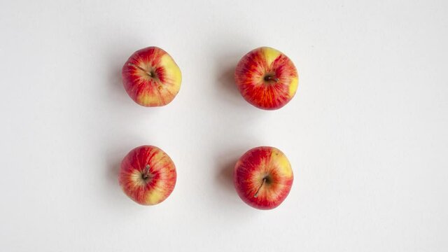Stop motion animation of a flat lay top view of four red autumn apples on midline that alternately disappear on white background. Healthy food and autumn mood concept.
