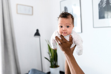 Cute baby girl in her father hands. Close up portrait of little daughter looking at the camera, family playing at home
