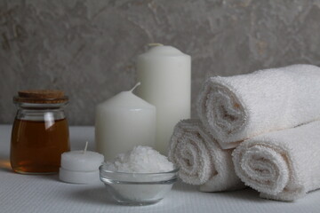 Obraz na płótnie Canvas Spa relax massage home care for soy body. White candles towels oil in a jar bottle scrub on a white gray background with space for text. Beauty parlour