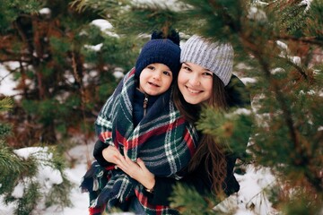 Mom and little son in the winter forest. Older sister and little brother hug. Winter day in the woods
