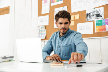 Fototapeta na wymiar Young brunette man working with laptop while sitting at desk in office