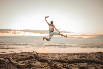 Fototapeta na wymiar Happy boy enjoying summer holidays on beach at sunset - Young man jumping on the beach at the sunrise - Vacations concept