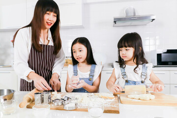 Smiling young mom teaching little daughter doing bakery at home kitchen