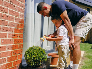 Father assisting son watering plant in back yard