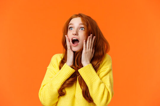 Oh No Something Falling From Sky. Shocked And Speechless, Startled Young Concerned Redhead Woman Drop Jaw, Gasping And Staring Upper Left Corner Concerned, Touching Face Worried, Orange Background