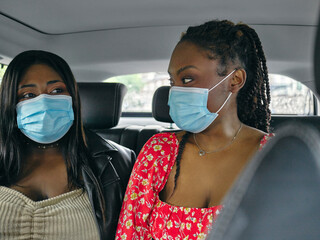 Two women in face masks on back seat of car