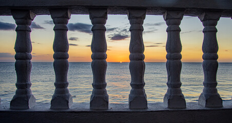 A colorful sunset seen  through balustrades on a beachfront balcony. Rincon, Puerto Rico.	
